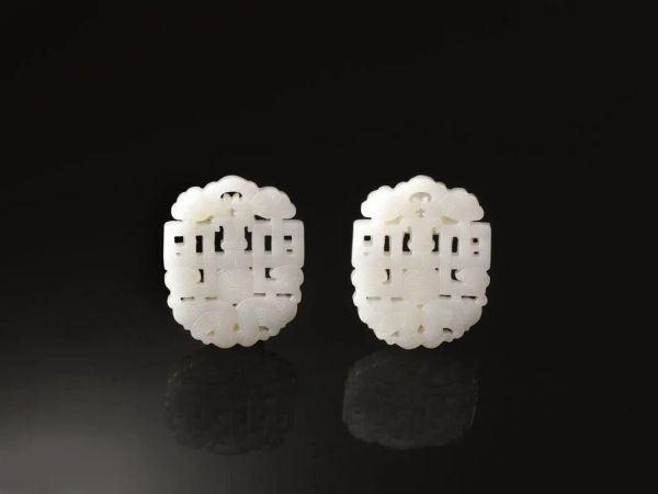  Coppia di intagli Cina sec. XX,  in giada bianca di forma ovoidale decorati con motivi geometrici a traforo e sormontati da due volatili stilizzati, 6,5x5,5 ciascuno (2)