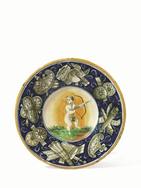  Piatto, Casteldurante, sec. XVI,  in maiolica decorata nel cavetto con figura di Cupido e tesa fondo blu a trofei d&rsquo;armi sui quali si legge Amor 1544, diam. cm 24