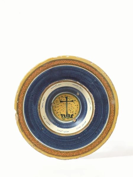 Piatto, Faenza, inizi sec. XVI, in maiolica decorata nei toni del blu e giallo ocra, cavetto col simbolo di San Bernardino, ampia tesa a motivi geometrici, diam. cm 21, restauri