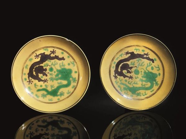  Coppia di piattini, Cina, marchio e periodo Guanxu (1875-1908),  in porcellana gialla, decorati da draghi color melanzana e verde al fronte, e tralci di vite al recto, diam cm 12,8,  uno con sbeccatura  (2)