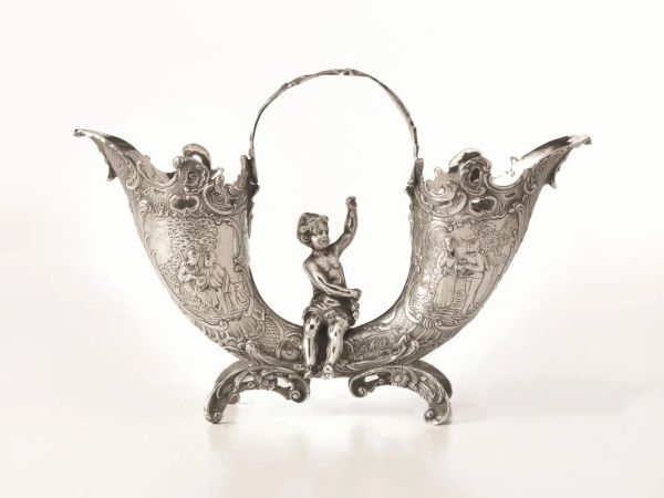 Portafiori centrotavola, in argento, realizzato come due cornucopie sbalzate a scene di genere, al centro un putto seduto, quattro piedini a volute, alt. cm 18, g 640