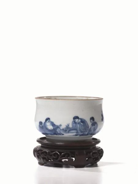  Ciotola Cina sec. XVII-XVIII , in porcellana bianca e blu, il bordo finemente inciso a motivi floreali, il corpo decorato con figure in un paesaggio, diam. cm 10,5, alt. cm 6,7, poggiante su base in legno 