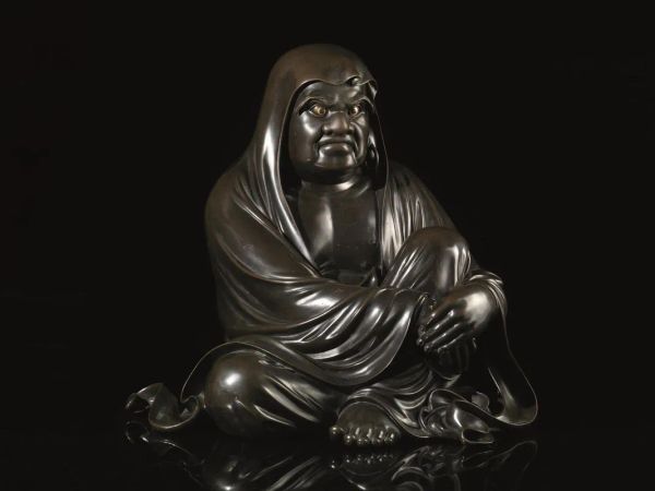  Scultura, Giappone fine periodo Meiji o inizi Taisho, circa 1900-1920 di Takahashi Ryoun , in bronzo raffigurante il Daruma, seduto in posizione rilassata, la gamba sinistra piegata e le mani incrociate sul ginocchio, coperto da una veste avvolgente e con occhi dorati e dallo sguardo imperioso, le grandi orecchie con orecchini movibili, il sotto della scultura Ã¨ dettagliato e mostra i piedi e la veste ripiegata, reca il marchio dell'artista, alt. cm 49