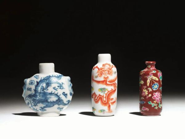  Tre snuff-bottles, Cina sec. XIX-XX , in porcellana, una a fondo bianco, decorata con dragoni rossi, una a fondo rosso decorata a fiori e farfalle, una bianca e blu con decoro a draghi, alt. cm 7,4; cm 6,4; cm 6,5 (3)