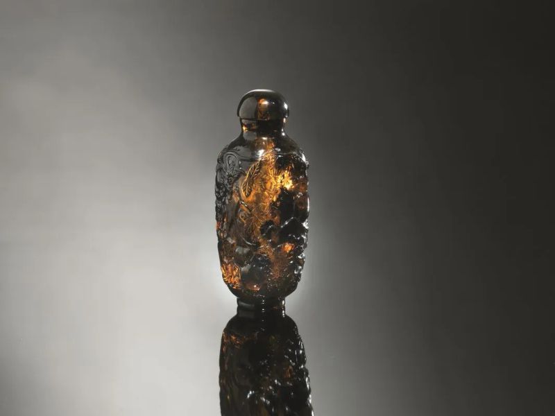  Snuff-bottle, Cina  inizi sec. XX,  in ambra intagliata, a forma di vaso squadrato e decorata a rami di pesco in fiore, alt. cm 7   - Auction Oriental Art - Pandolfini Casa d'Aste
