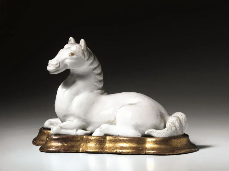 Cavallo Cina sec. XX , in porcellana bianca, in posizione accucciata, e poggiante su base in legno dorato, lung. cm 23  - Asta Arte Orientale - Pandolfini Casa d'Aste