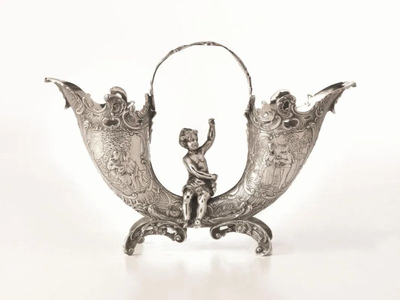 Portafiori centrotavola, in argento, realizzato come due cornucopie sbalzate a scene di genere, al centro un putto seduto, quattro piedini a volute, alt. cm 18, g 640  - Asta Argenti e Numismatica - II - Pandolfini Casa d'Aste